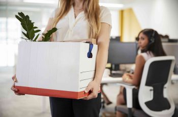 mulher carregando uma caixa com suas coisas após demissão da empresa